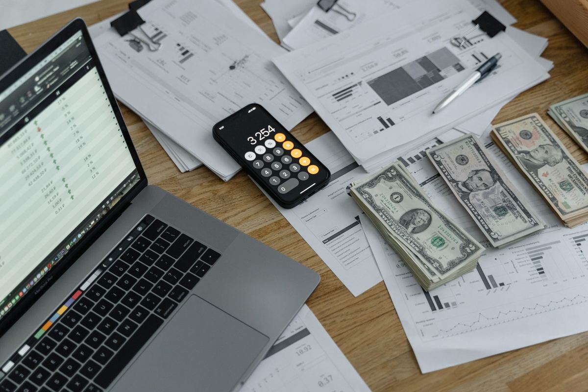 Laptop spreadsheet, calculator and cash on a desk